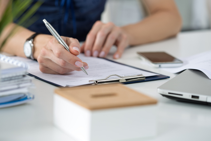 Woman writing on document attached to clipboard
