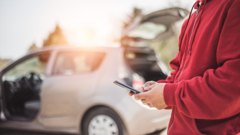 Man in red sweatshirt texting after a car accident.