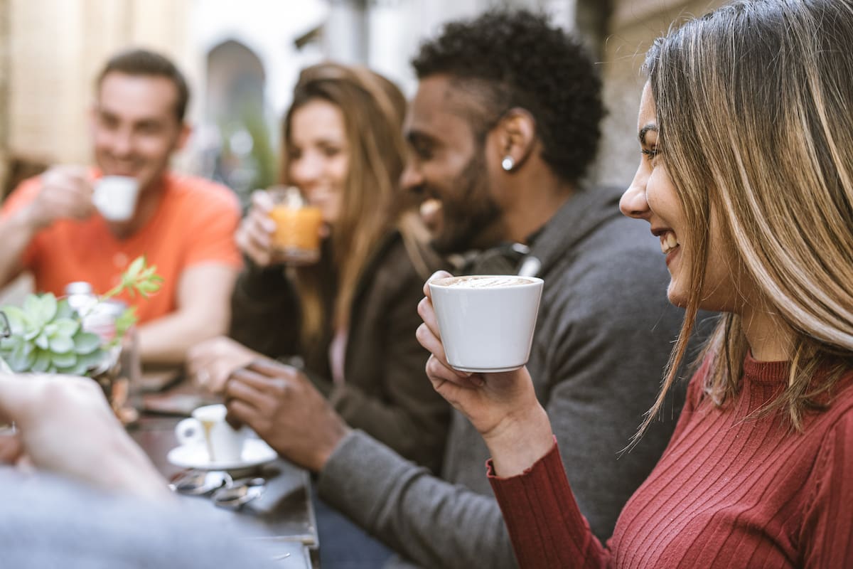 Group of young people friends enjoying breakfast at outdoors restaurant having fun talking