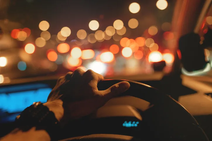 a man's hand on a steering wheel driving at nighttime