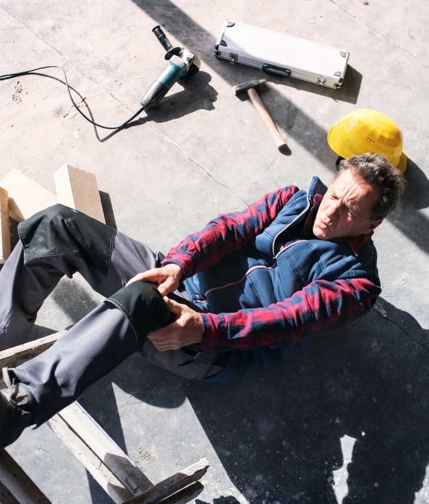 Un trabajador se cae de una escalera en una obra y se agarra la rodilla dolorido