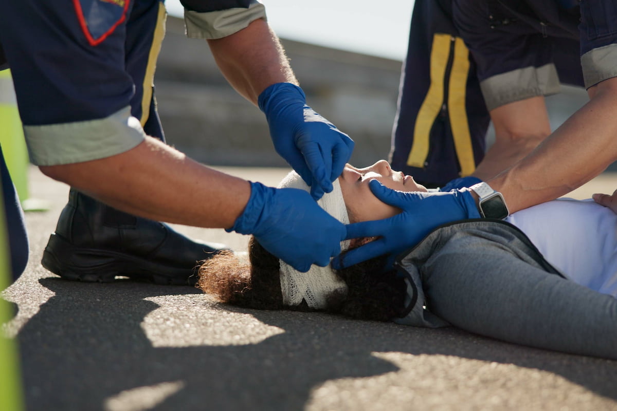 Mujer con una herida en la cabeza tendida en la carretera y recibiendo tratamiento médico de urgencia por parte de los paramédicos.