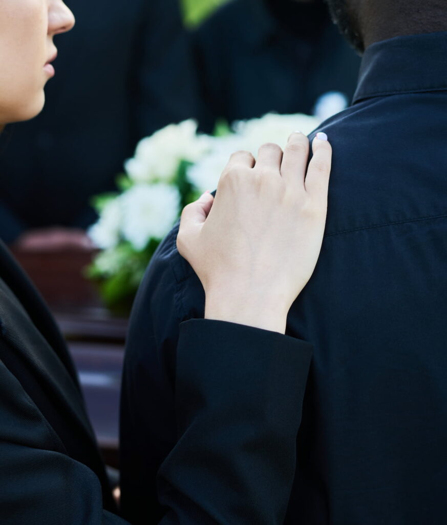 Woman placing her hand on a man's shoulder comforting him at a funeral 