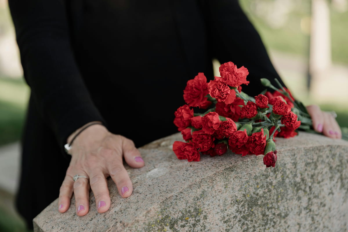 Woman wearing a wedding ring placing red flowers on a grave