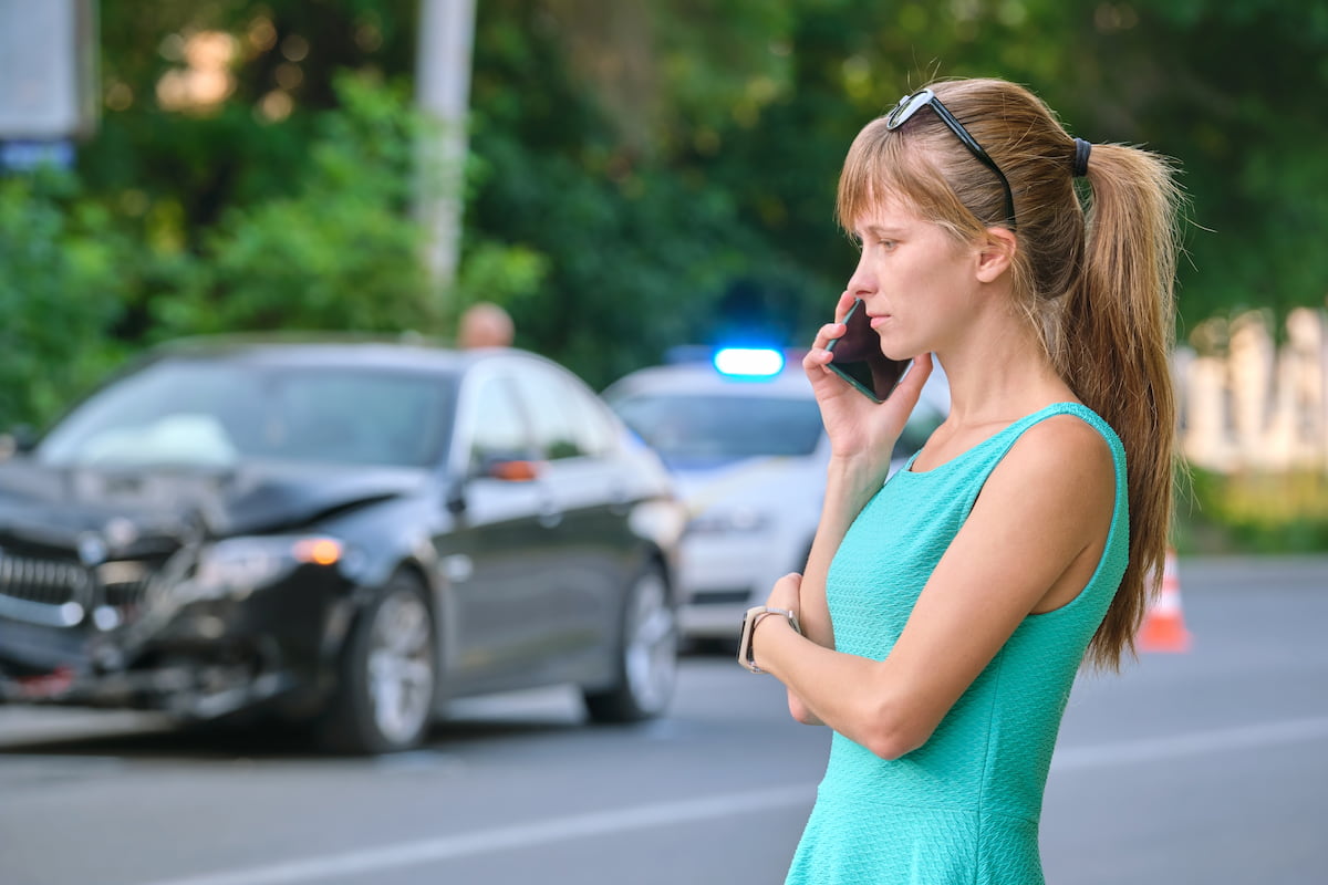A women in a green dress talking on the phone after a car accident.