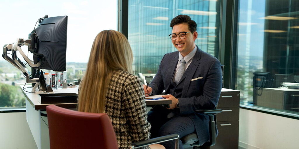 Daniel Kim sitting at his desk talking to a female client with her back turned toward the camera