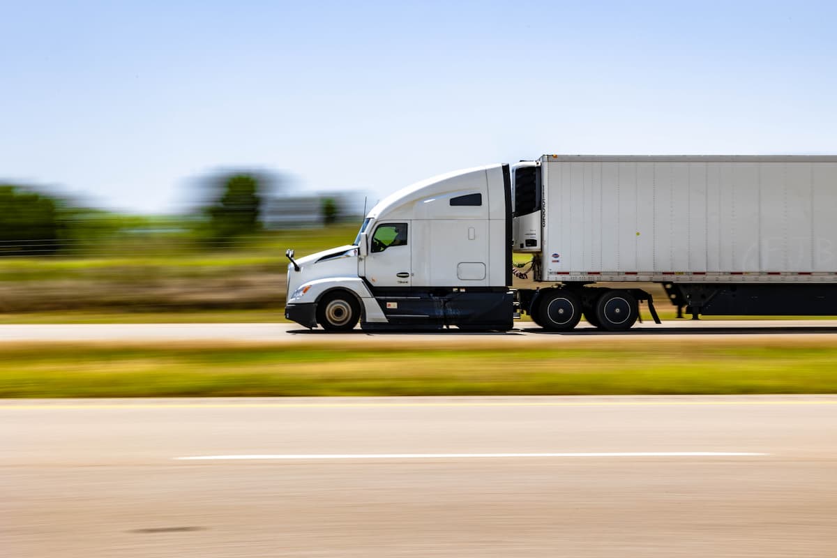 A semi truck driving on a rural road with trees in the background
