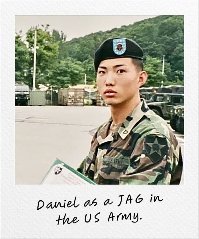 Young Daniel Kim in military uniform and beret while serving as a JAG officer in the U.S. Army, holding a document folder. Handwritten text on the photo reads 'Daniel as a JAG in the US Army.