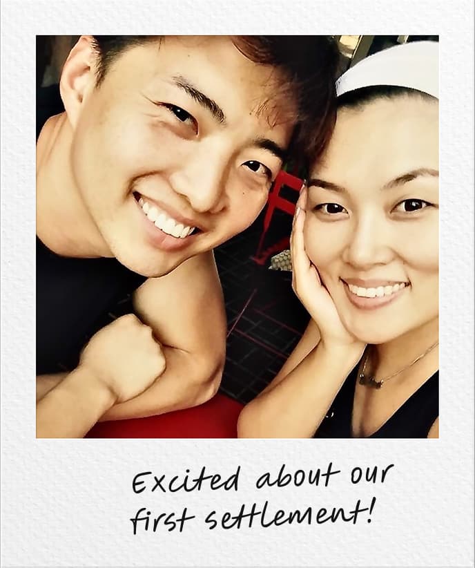 Smiling couple taking a close-up selfie, with handwritten text at the bottom reading 'Excited about our first settlement!