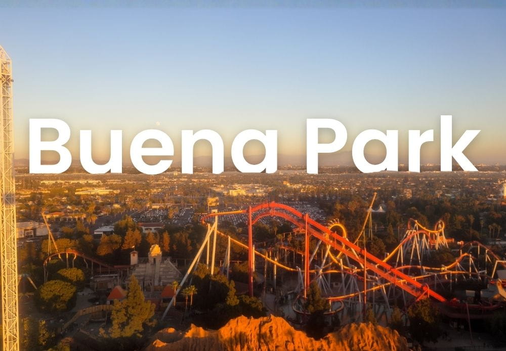 Aerial view of Buena Park with a roller coaster and surrounding city under a warm sunset sky.