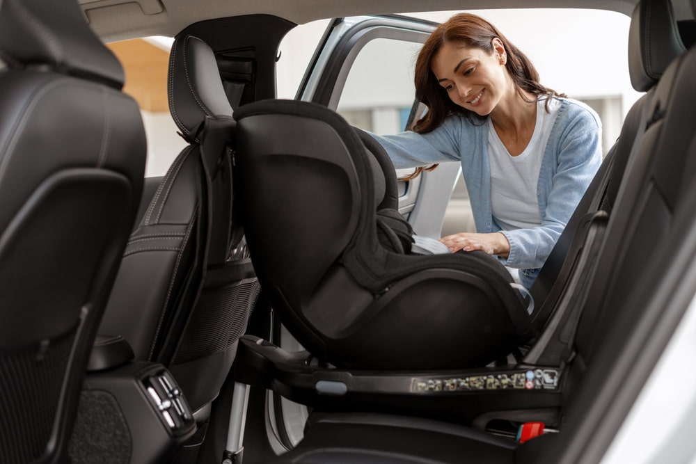 Smiling mother fastening and securing child safety seat inside car, ensuring safe travel for children