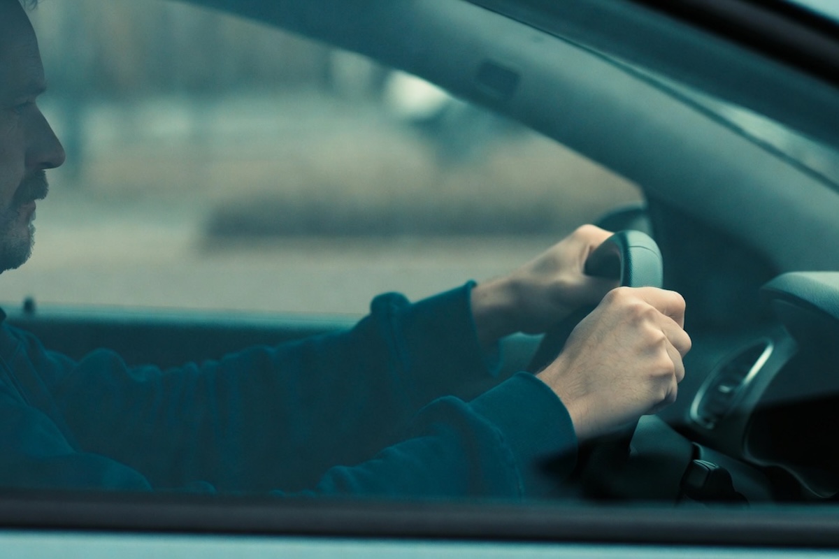 A man grips the steering wheel anxiously while sitting inside his vehicle.