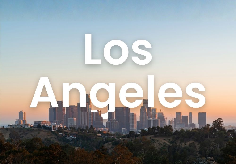 Los Angeles skyline at sunset with downtown buildings and hills in the foreground under a warm evening sky.