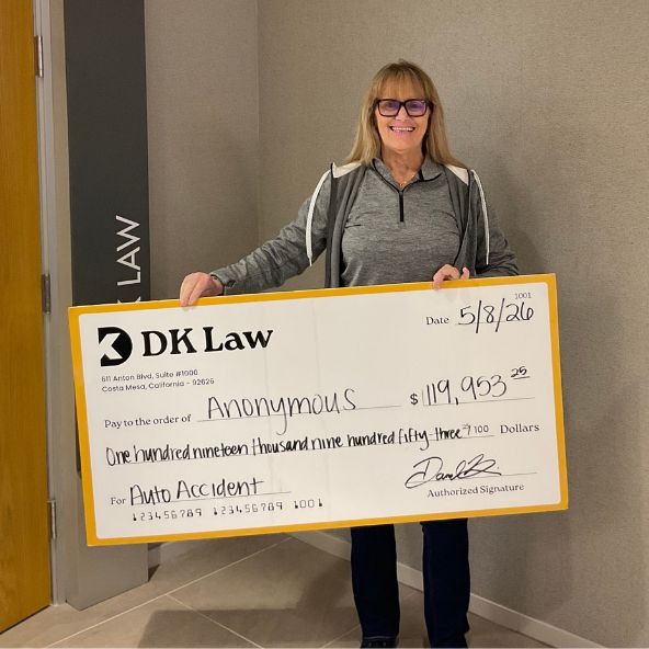 An individual holding a large DK Law Settlement Check for an auto accident case & the amount being $119,953.