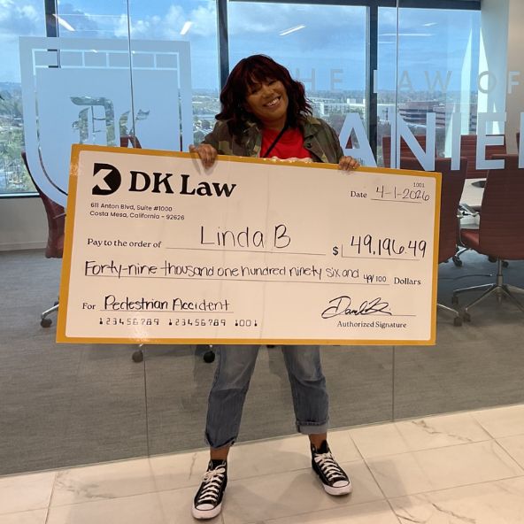 A DK Law client stands holding a large check from DK Law for $49,196.99.