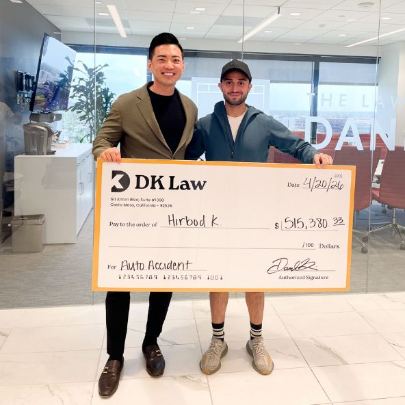 Daniel Kim and DK Law clientn stand in DK Law office holding an oversized DK Law settlement check for an auto accident case, with the check showing a $515,380.33 payout.