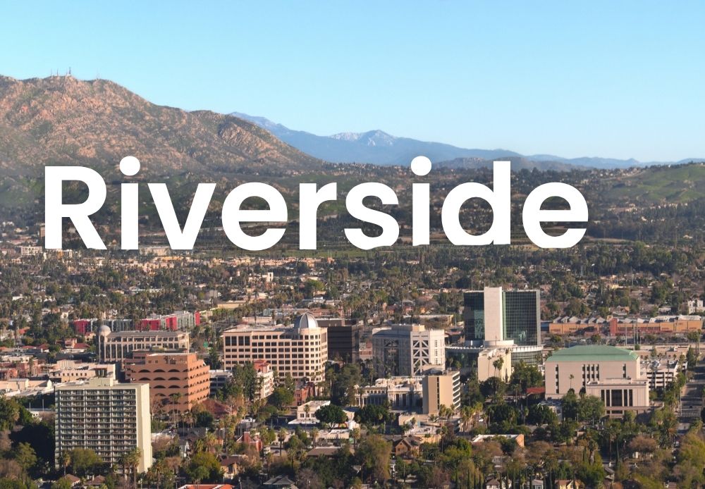 Aerial view of downtown Riverside with mountains in the background and large white text reading “Riverside.”