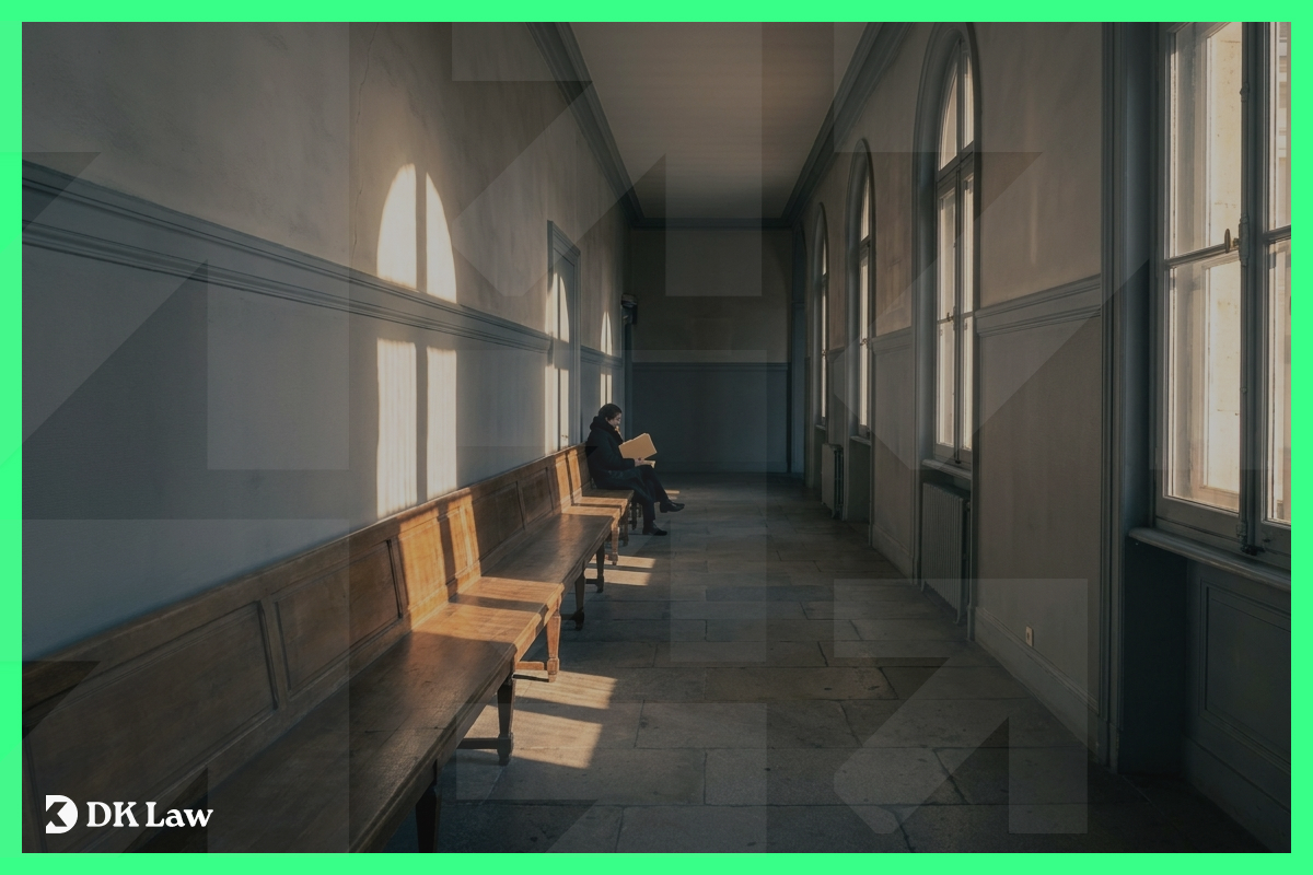 Person sitting alone on a bench in a long courthouse hallway